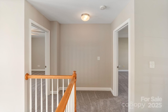 hallway with carpet floors, baseboards, and an upstairs landing