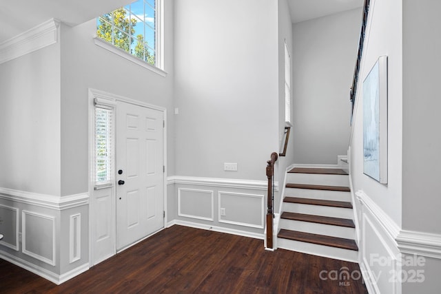 entrance foyer with dark wood finished floors, a decorative wall, stairs, and a wainscoted wall