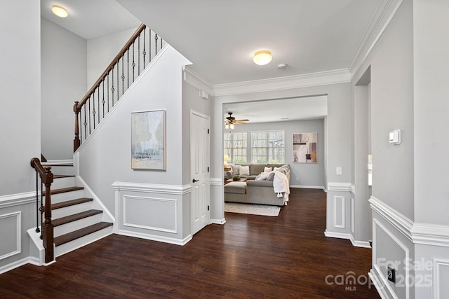 foyer entrance with crown molding, stairway, a decorative wall, and wood finished floors