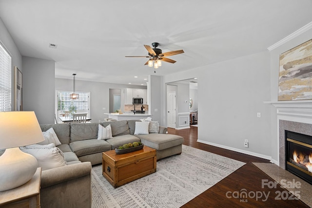 living room with visible vents, dark wood-type flooring, baseboards, a fireplace with flush hearth, and a ceiling fan