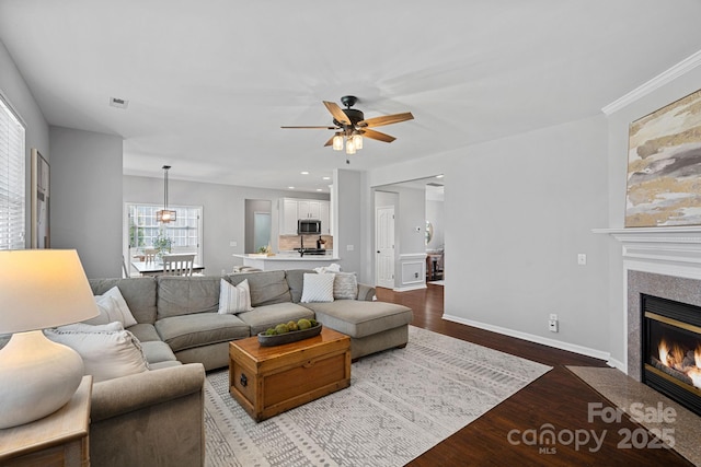 living room with a ceiling fan, visible vents, baseboards, a fireplace with flush hearth, and dark wood-type flooring