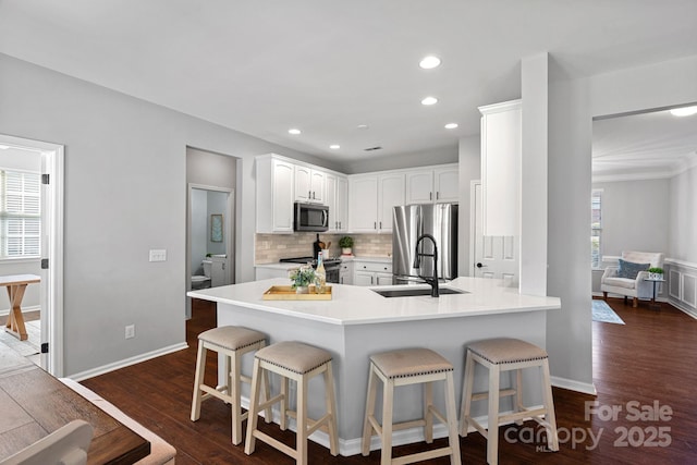 kitchen with dark wood-style floors, a breakfast bar, a peninsula, stainless steel appliances, and decorative backsplash