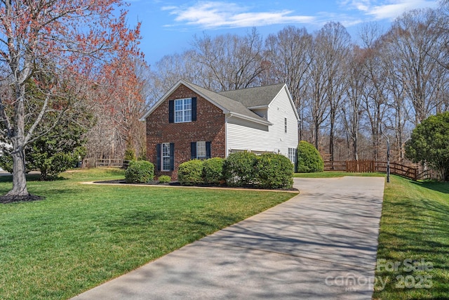 view of side of property with brick siding, a lawn, driveway, and fence