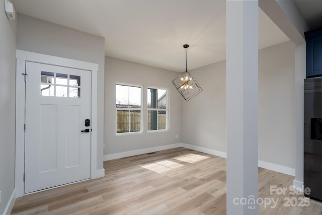 foyer featuring baseboards, light wood-type flooring, and an inviting chandelier