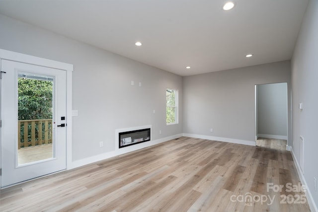 unfurnished living room featuring light wood finished floors, recessed lighting, baseboards, and a glass covered fireplace