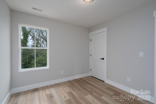 empty room featuring light wood finished floors, plenty of natural light, visible vents, and baseboards