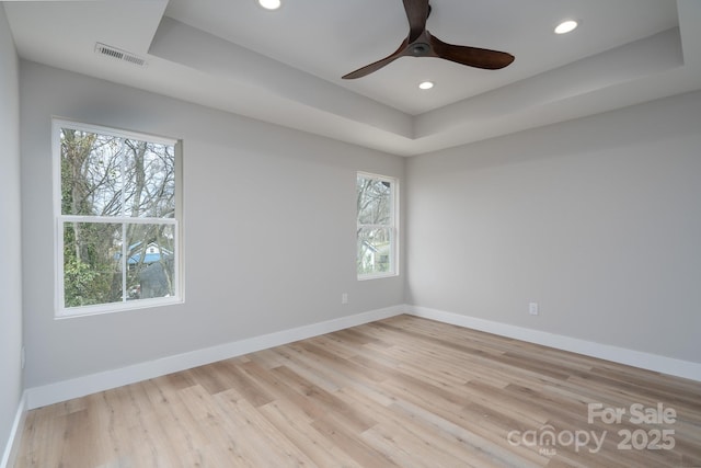 spare room with baseboards, visible vents, a tray ceiling, and wood finished floors