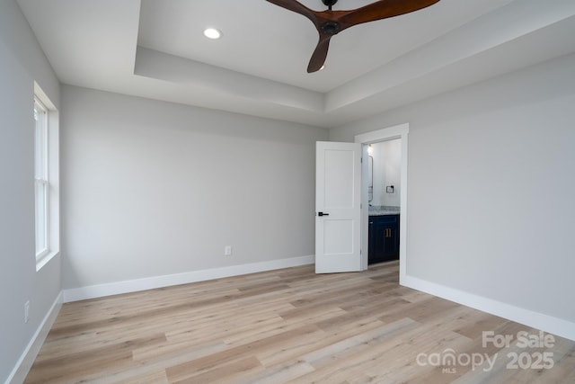 spare room featuring light wood-style floors, a tray ceiling, and baseboards