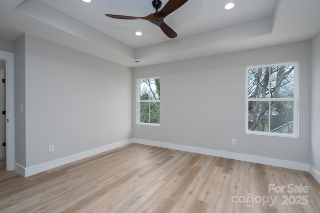 spare room with light wood-style floors, recessed lighting, a raised ceiling, and baseboards