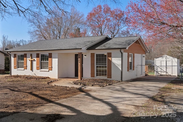 ranch-style home featuring an outbuilding, driveway, a shed, roof with shingles, and brick siding