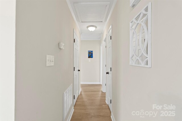 corridor with visible vents, light wood-style floors, crown molding, baseboards, and attic access