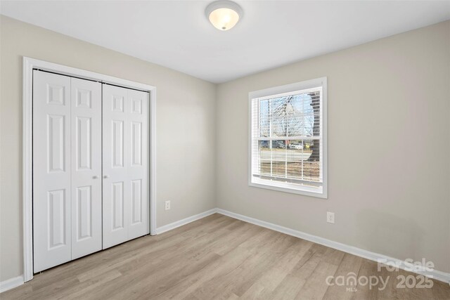 unfurnished bedroom with a closet, light wood-style flooring, and baseboards