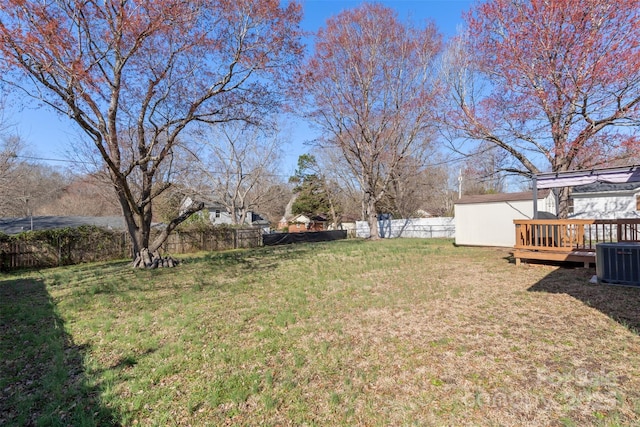 view of yard featuring fence, a shed, a wooden deck, central AC, and an outbuilding