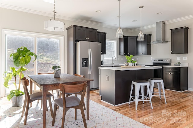 kitchen featuring wall chimney exhaust hood, a kitchen island, stainless steel appliances, light countertops, and light wood-type flooring