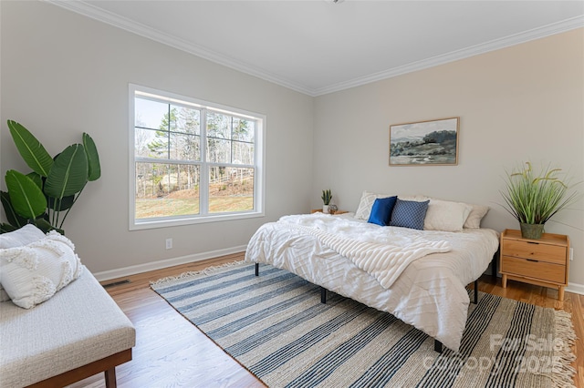 bedroom with baseboards, visible vents, crown molding, and wood finished floors