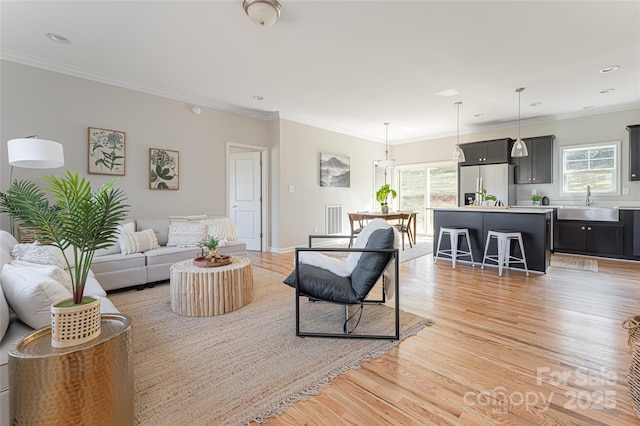 living area with ornamental molding, light wood-type flooring, visible vents, and recessed lighting