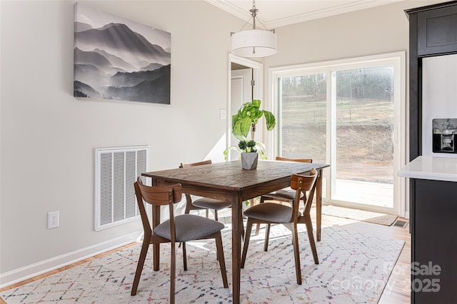 dining room featuring baseboards, visible vents, light wood-style flooring, and crown molding