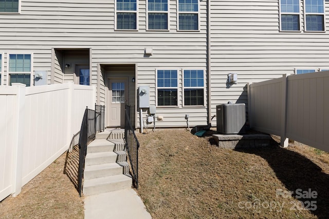 view of exterior entry with central AC unit and fence