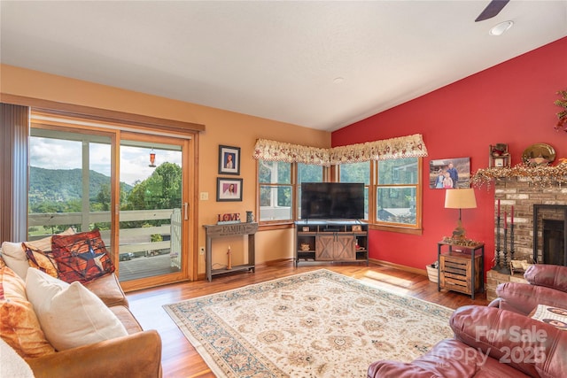 living area featuring a healthy amount of sunlight, a brick fireplace, vaulted ceiling, and wood finished floors