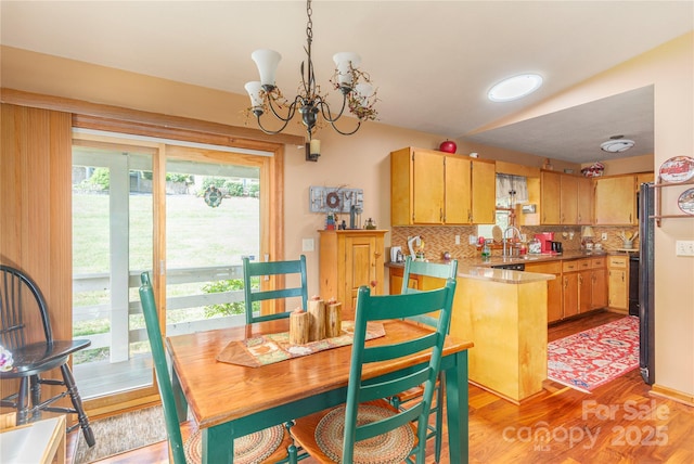 kitchen with light wood finished floors, decorative backsplash, a peninsula, a notable chandelier, and a sink