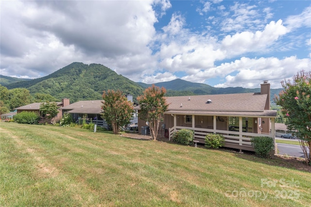 back of property featuring a chimney, roof with shingles, a yard, a mountain view, and board and batten siding