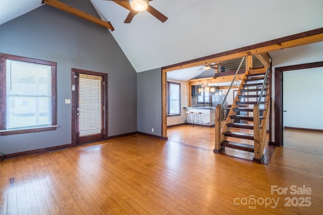 unfurnished living room with beam ceiling, wood-type flooring, high vaulted ceiling, baseboards, and stairs