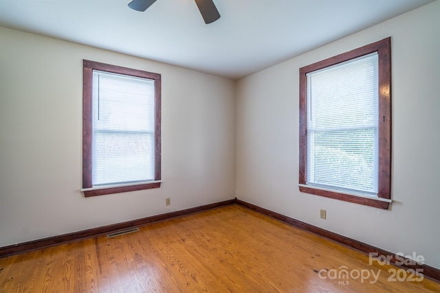 unfurnished room featuring light wood-style floors, a wealth of natural light, visible vents, and baseboards