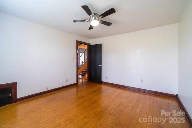 empty room featuring hardwood / wood-style flooring, ceiling fan, stairway, and baseboards