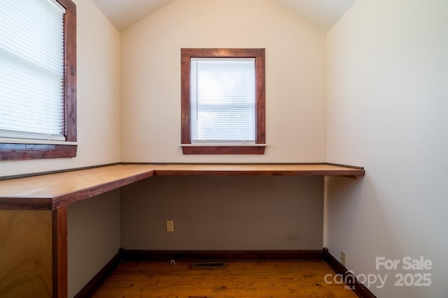 unfurnished office featuring visible vents, vaulted ceiling, built in desk, and wood finished floors