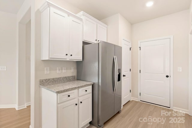 kitchen featuring stainless steel fridge with ice dispenser, light wood-style flooring, white cabinetry, light stone countertops, and baseboards