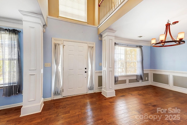 foyer entrance with decorative columns, a decorative wall, hardwood / wood-style floors, and an inviting chandelier