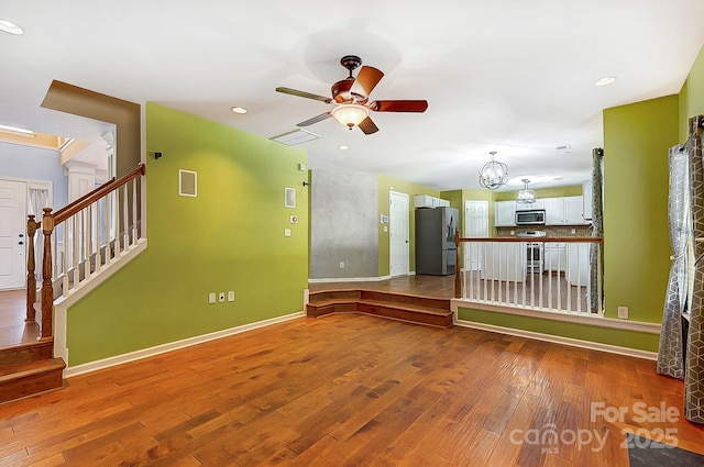 unfurnished room featuring baseboards, visible vents, wood-type flooring, stairs, and ceiling fan with notable chandelier