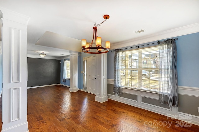 unfurnished dining area with hardwood / wood-style flooring, visible vents, ornamental molding, ornate columns, and an inviting chandelier