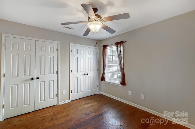 unfurnished bedroom featuring baseboards, wood finished floors, visible vents, and multiple closets