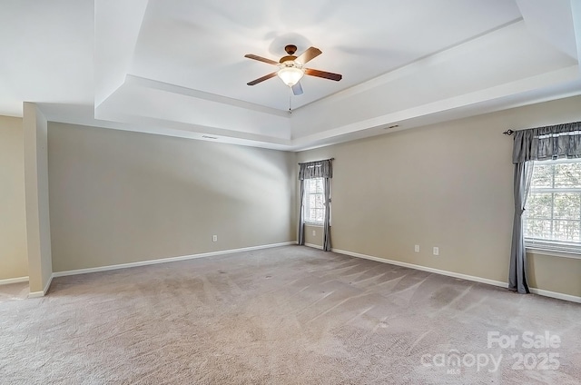 unfurnished room featuring carpet floors, a raised ceiling, plenty of natural light, and baseboards