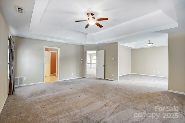 empty room featuring light carpet, baseboards, visible vents, a ceiling fan, and a tray ceiling