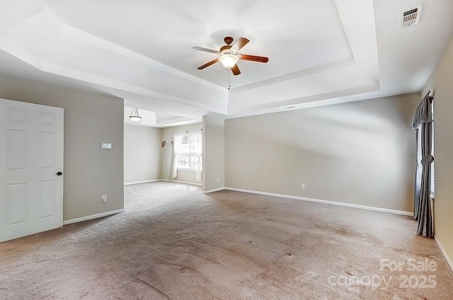 carpeted empty room featuring a ceiling fan, a raised ceiling, visible vents, and baseboards