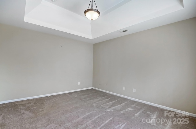 carpeted spare room featuring a raised ceiling, visible vents, and baseboards