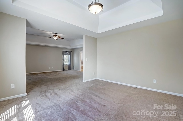 carpeted empty room featuring ceiling fan, a tray ceiling, and baseboards