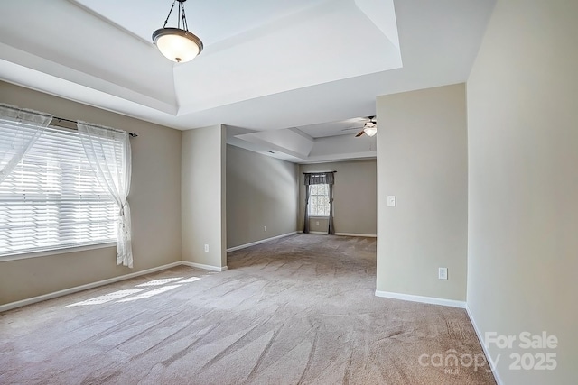 carpeted spare room featuring a tray ceiling, ceiling fan, and baseboards