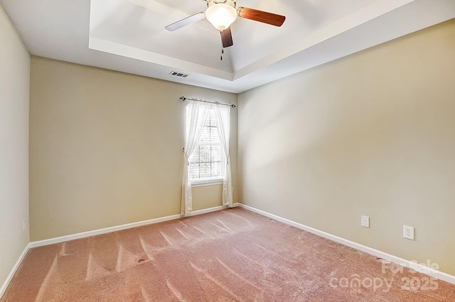 empty room featuring a tray ceiling, light colored carpet, visible vents, and baseboards