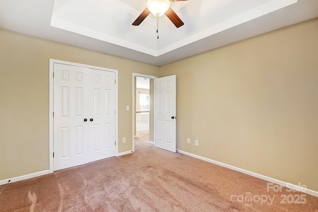 unfurnished bedroom with a closet, a raised ceiling, carpet flooring, and baseboards