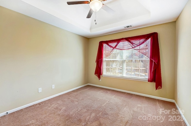 carpeted empty room with baseboards, visible vents, ceiling fan, and a raised ceiling