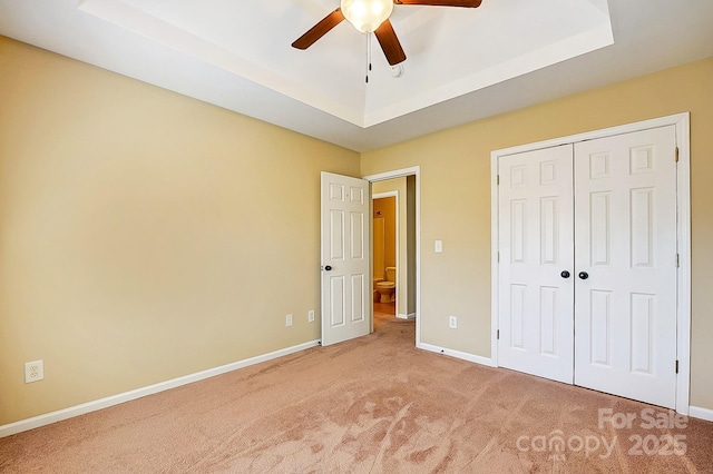 unfurnished bedroom featuring a closet, a raised ceiling, light colored carpet, and baseboards