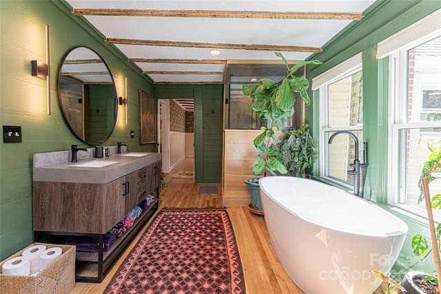 bathroom with a sink, a freestanding bath, wood finished floors, and double vanity