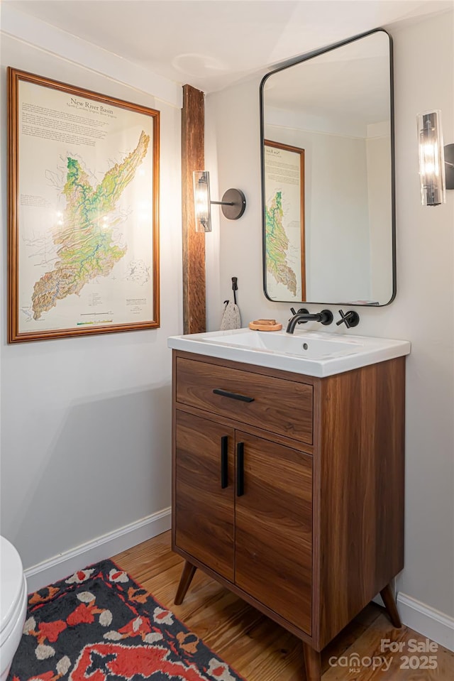 bathroom with toilet, vanity, baseboards, and wood finished floors