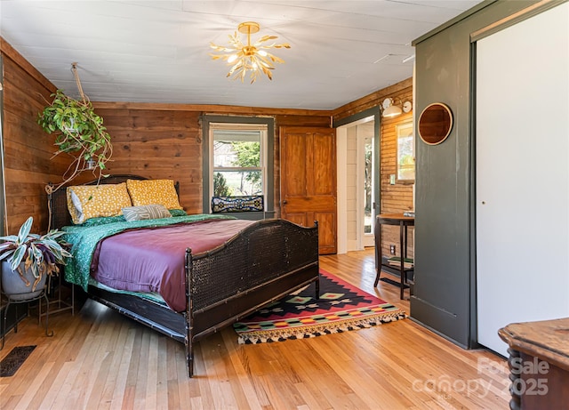 bedroom with hardwood / wood-style flooring, wooden walls, visible vents, and a chandelier