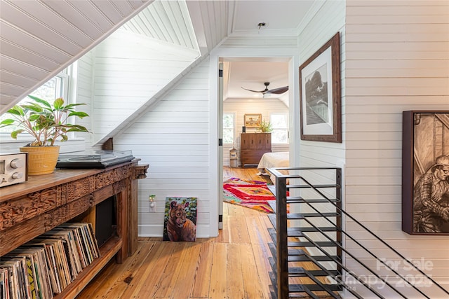 corridor with an upstairs landing, light wood-style floors, wood walls, and crown molding