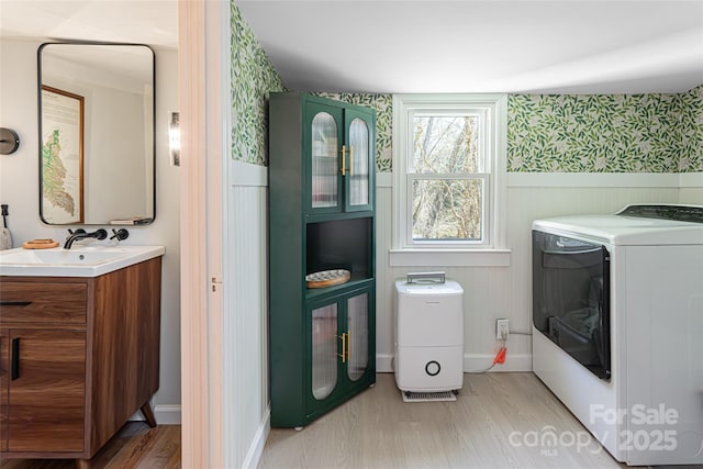 laundry area with light wood-type flooring, laundry area, wainscoting, washer / dryer, and a sink