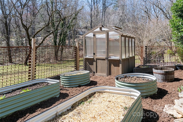 view of yard featuring a greenhouse, an outdoor structure, a vegetable garden, and fence